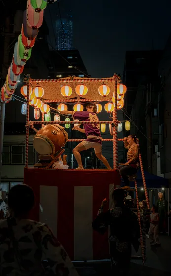 Spectators in yukata watching the float from below, lanterns above them