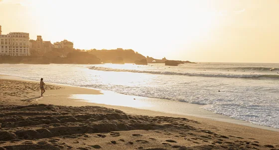One walker crossing the wet sand of an empty beach at sunset